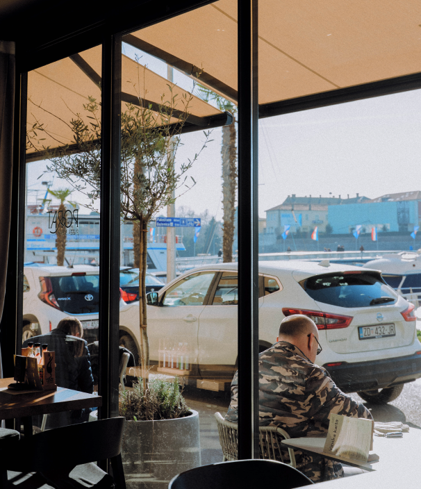Unutrašnjost Porat Pizza & Bar u Zadru s pogledom na rivu, more i logo na staklu; gost uz vinsku kartu
